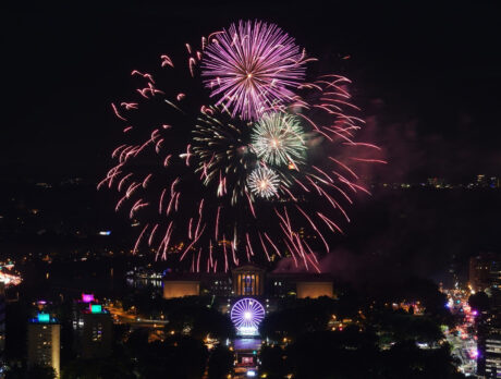 A glowing fireworks display explodes over the Philadelphia Museum of Art and Benjamin Franklin Parkway in a night sky.