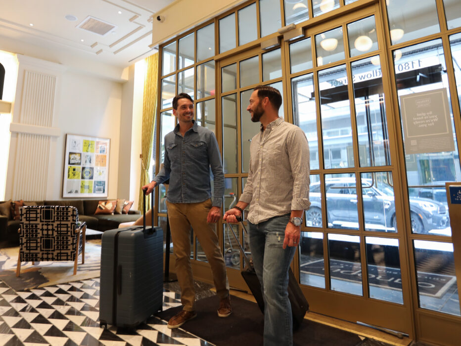 Two people with suitcases walk through glass doors into the lobby at Canopy by Hilton Philadelphia.