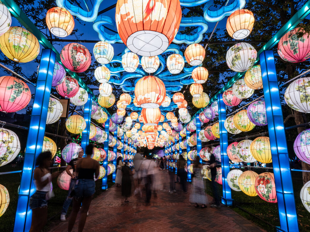 Visitors walk through a glowing tunnel of colorful, ornate paper lanterns at the Chinese Lantern Festival, creating a dazzling tunnel of light.