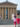Visitors walk up the iconic stone steps outside the Philadelphia Museum of Art. The massive building, with tall columns and triangular pediment, rides in front of them as people sit and stand around the fountain the courtyard.