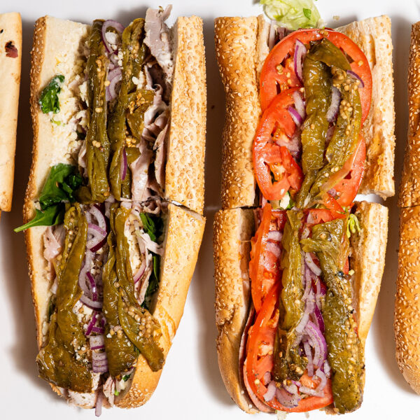 An overhead view of four hoagies from Fink's Hoagies, each filled with a variety of meats, cheeses, vegetables and toppings on sesame seed rolls.
