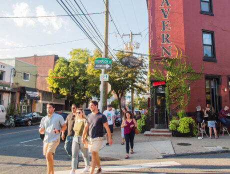 People cross a street in the heart of Fishtown, passing local bars and restaurants on a sunny day.