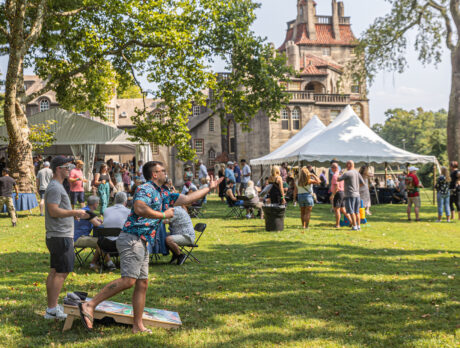 Festivalgoers sip drinks and play lawn games beneath shady trees on a grass lawn in front of Fonthill Castle during the annual beer fest.