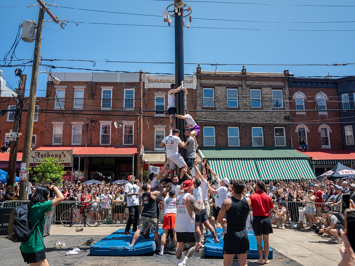 Crowds cheer as a team climbs a greased telephone pole during the annual Italian Market Festival on South 9th Street in Philadelphia.