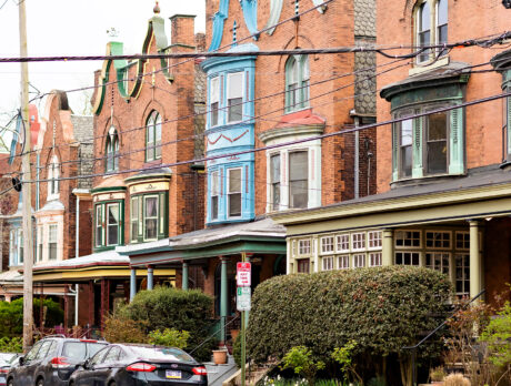 A row of brick Victorian homes with colorful and ornate accents line a residential street in West Philadelphia.