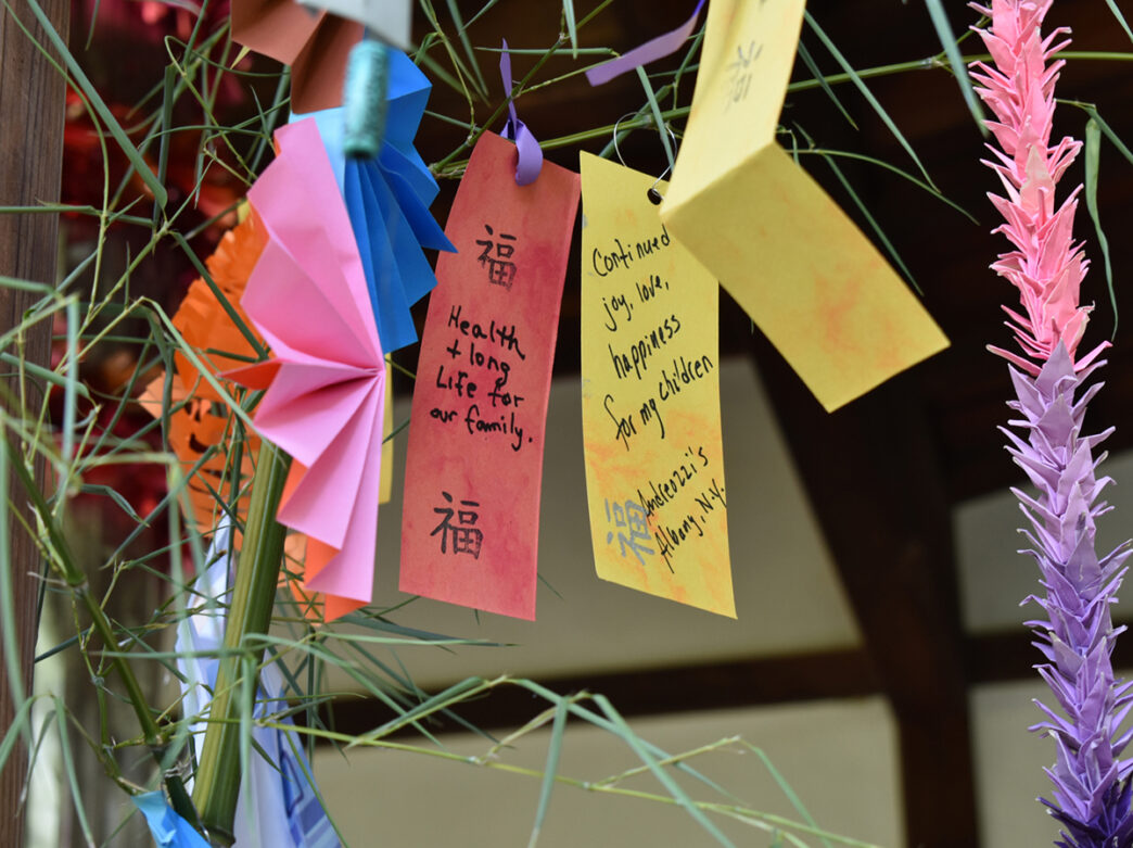 A close-up of handwritten wish cards and colorful paper decorations hanging from bamboo branches during the Tanabata Festival at Shofuso Japanese Cultural Center.