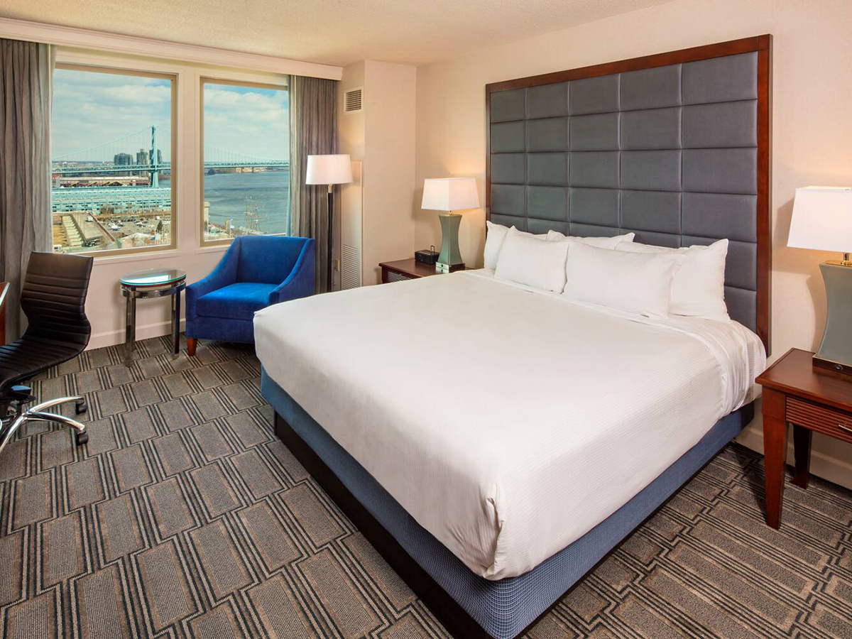 A modern hotel room with a king bed and large windows with views of the Delaware River.