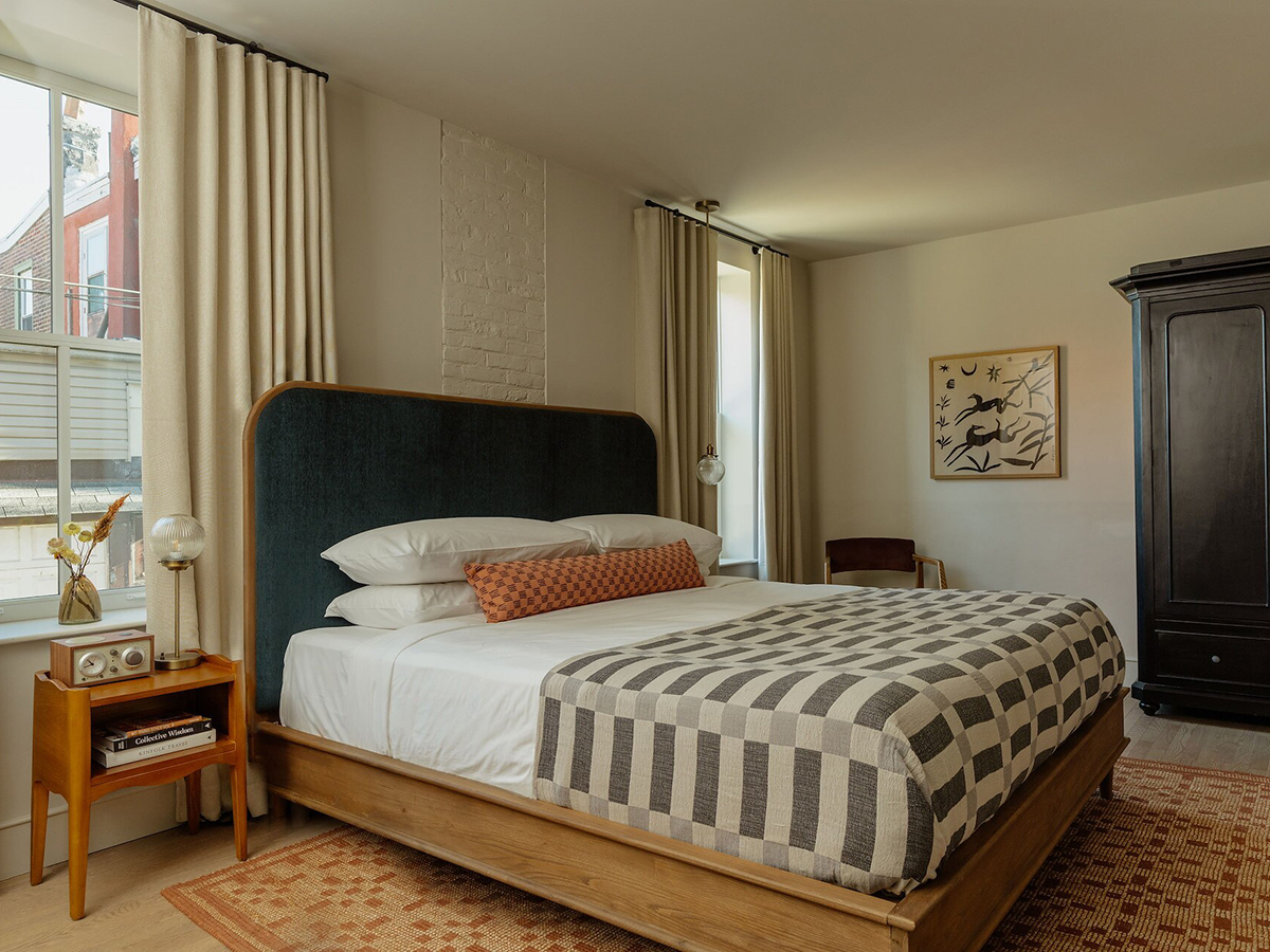 A cozy, modern guest room at Hotel Anna & Bel, featuring minimalist décor, a checkered duvet and soft natural light from tall windows.