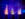 Three members of the Blue Man Group drum as colorful liquid splashes into the air off the drums under dramatic stage lighting.