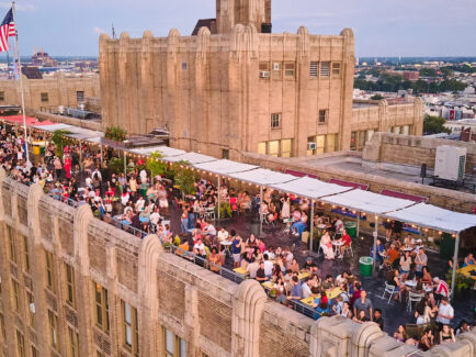 A rooftop packed with people dining and drinking at Bok Bar, with string lights, trees and city views in the background.