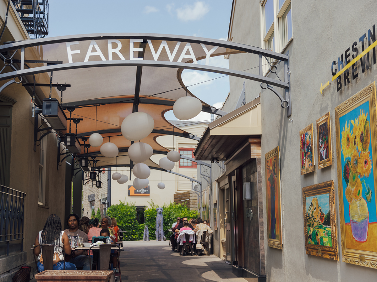 People dining outdoors in an alleyway under a canopy with round, white lanterns at the Market at the Fareway.