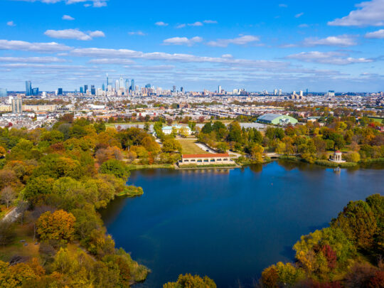 An aerial view of FDR Park in South Philadelphia, with tree-lined streets, a lake and the Center City skyline in the distance.