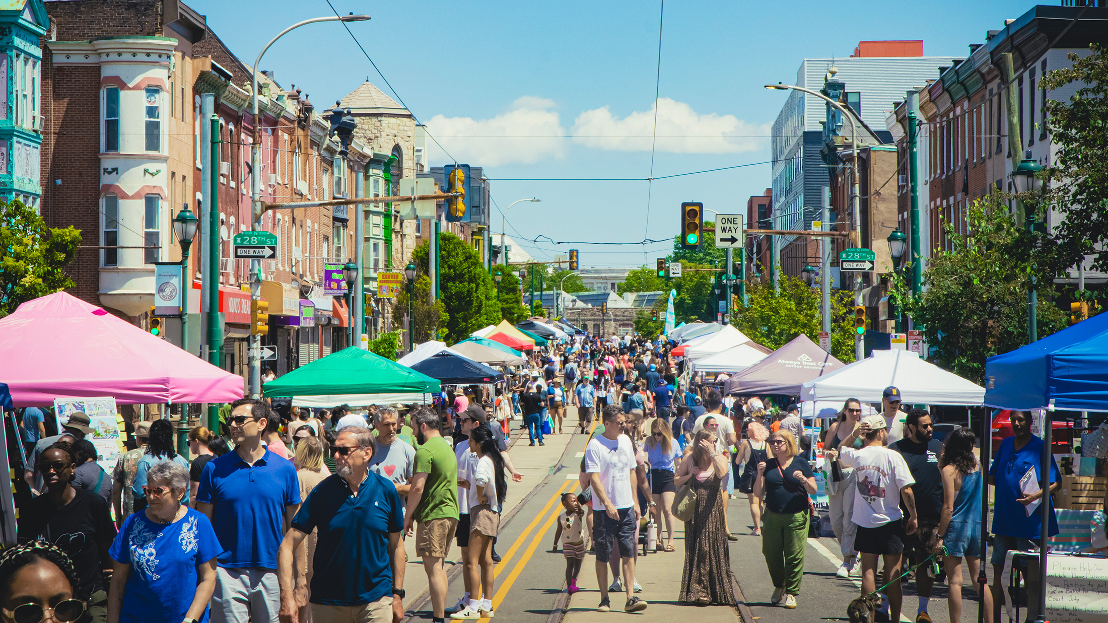 Crowds stroll along a closed-off street lined with colorful vendor tents and historic brick buildings during the lively Girard Avenue Street Fest.