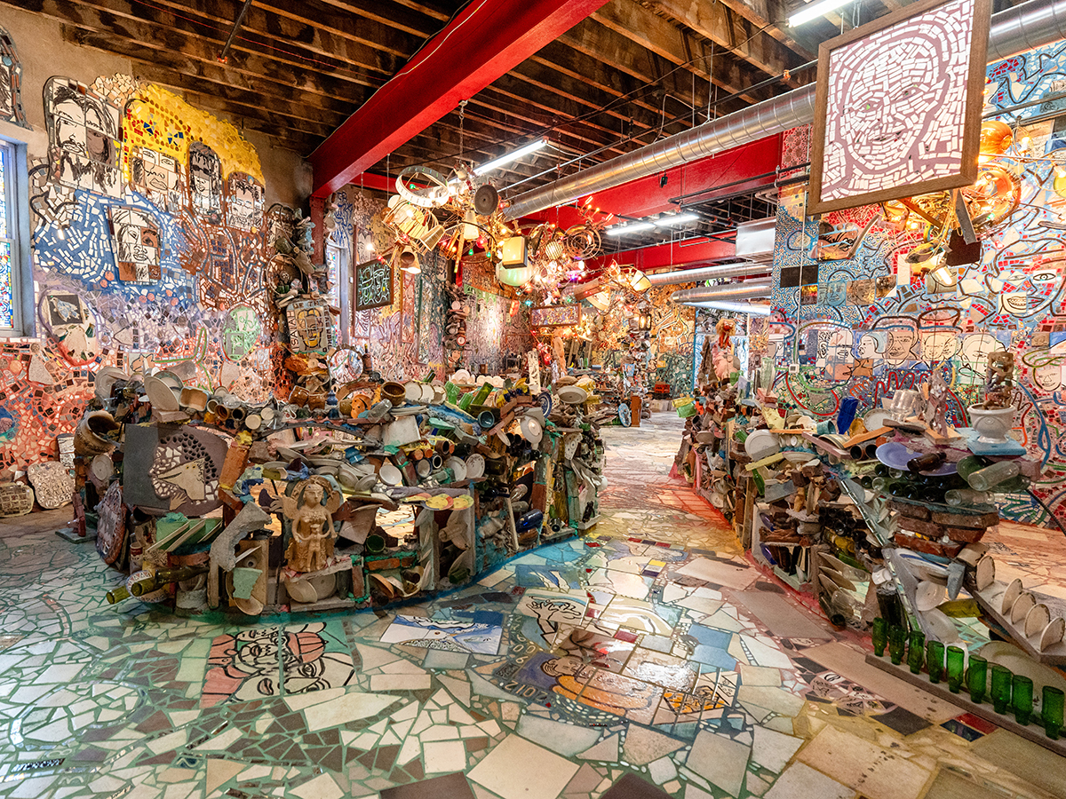 A colorful indoor space filled with Isaiah Zagar's mosaic art, covering the walls, floor and ceiling with tiles, bottles and other found objects.