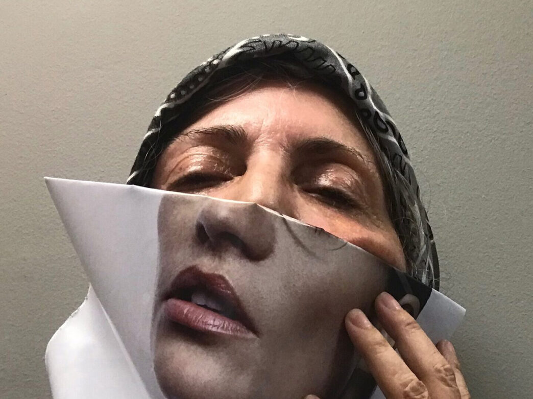A person holds up a printed image of lips and a nose over their face, blending it with their own features in a creative art piece.