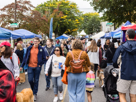 Crowds browse rows of colorful vendor tents on a closed-off street during the fall festival in Roxborough.