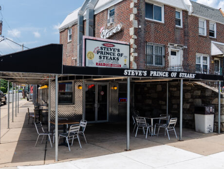 The exterior of the original Steve's Prince of Steaks in Northeast Philadelphia, with a black awning covering tables and chairs on the corner sidewalk.