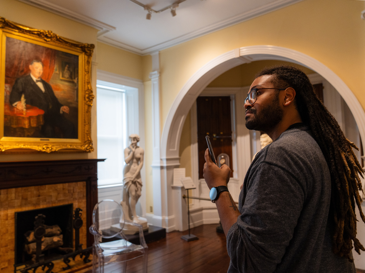 A visitors looks at and takes photos with their phone of the artwork on display inside the Woodmere.