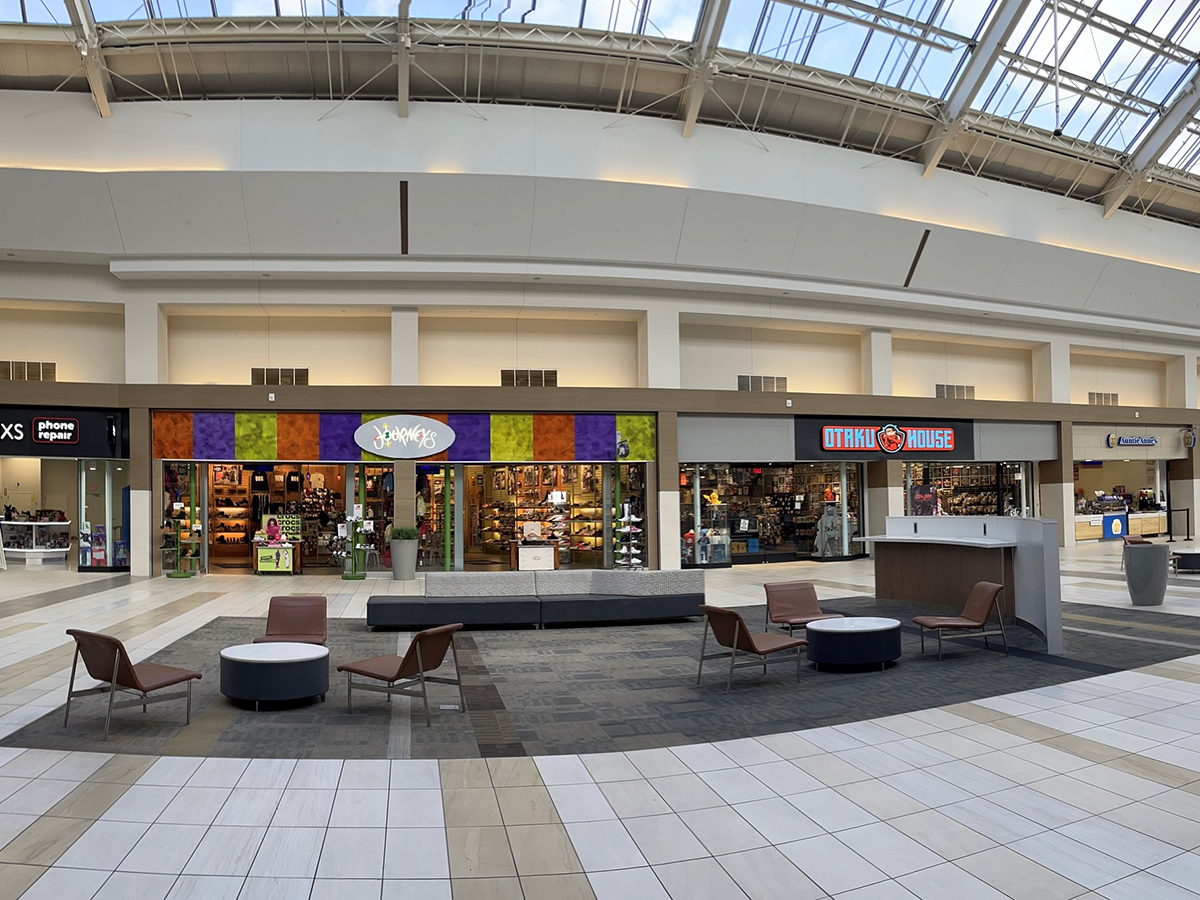 Interior of a mall with storefronts under a bright glass ceiling.