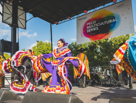 Bailarinas ataviadas con coloridos trajes tradicionales mexicanos giran en el escenario bajo una pancarta de "PECO Multicultural Series".
