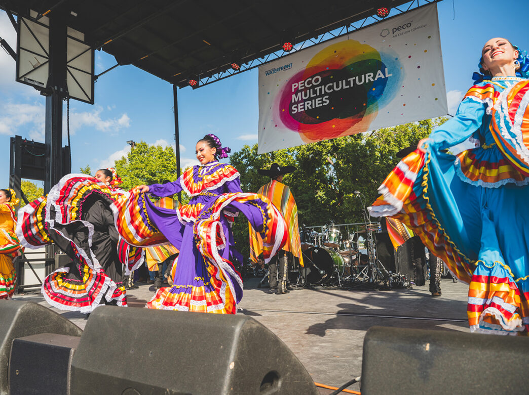 Performers in vibrant traditional Mexican dresses twirl during a folklorico dance performance on stage during the Mexican Independence Day Festival.