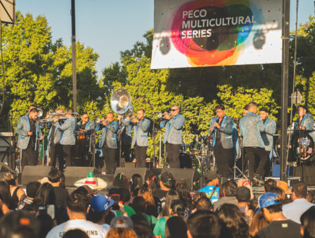 A mariachi band in matching blue jackets performs on stage before a large crowd at the Mexican Independence Day celebration.