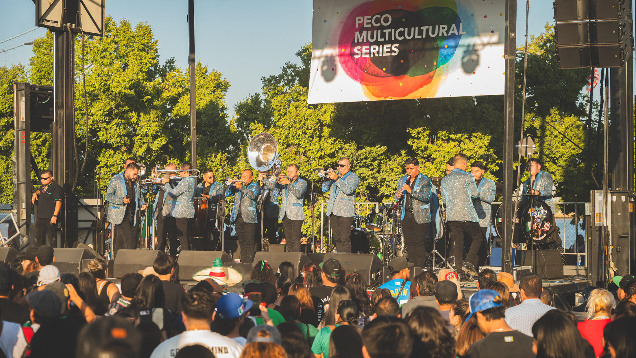 A mariachi band in matching blue jackets performs on stage before a large crowd at the Mexican Independence Day celebration.
