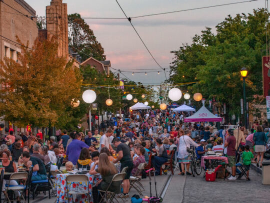 Multitudes llenan una calle sin coches de Mt. Airy para asistir a una Supper Session nocturna, con cena al aire libre y espectáculo en directo.