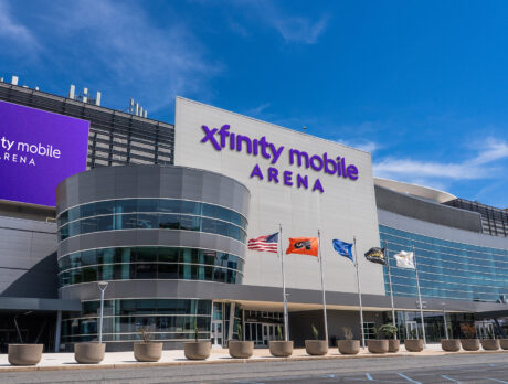A rendering of the sleek, modern Xfinity Mobile Arena with glass walls, flags flying out front and a bright purple marquee.