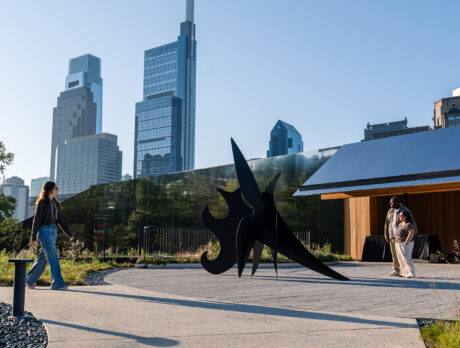 Visitors explore Calder Gardens, walking past a striking black outdoor sculpture framed by modern skyscrapers in the distance.