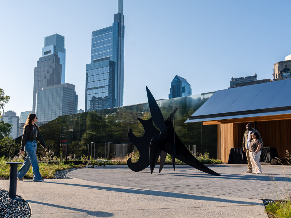 Visitors explore Calder Gardens, walking past a striking black outdoor sculpture framed by modern skyscrapers in the distance.