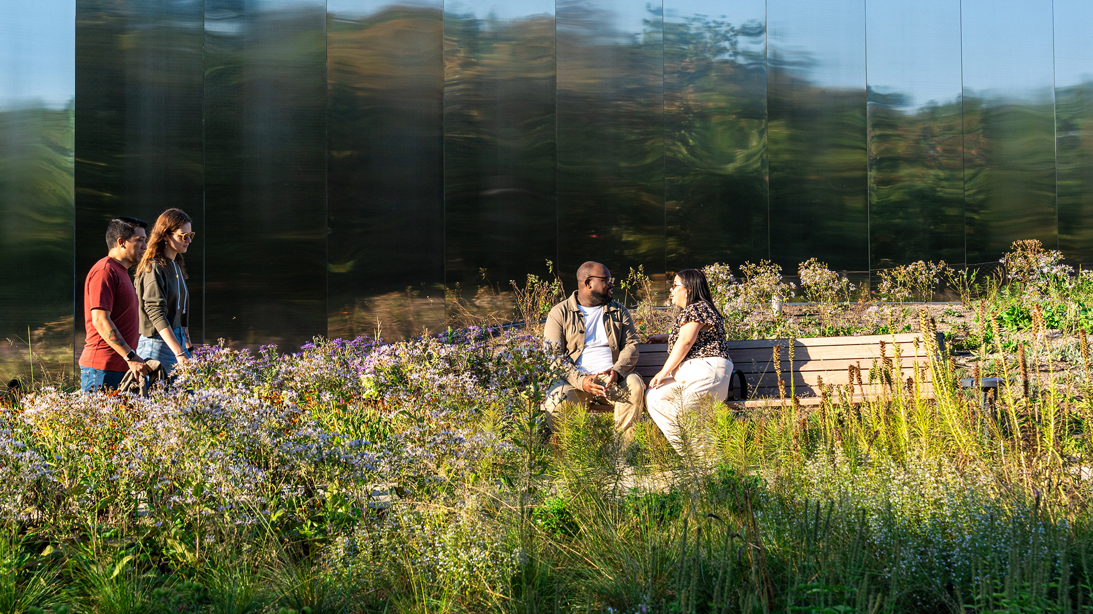Visitors enjoy Calder Gardens, with two people walking along a garden path while another pair sit on a bench surrounded by wildflowers.