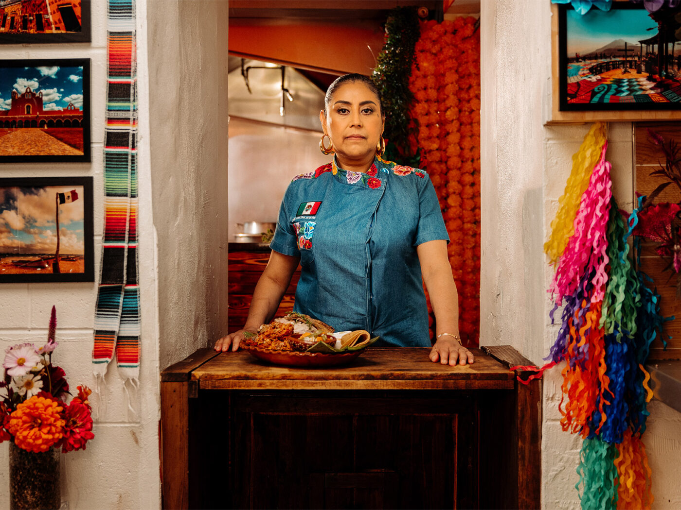 Chef Cristina Martinez stands behind a table inside her restaurant. On the table in front of her sits a Mexican dish she created.