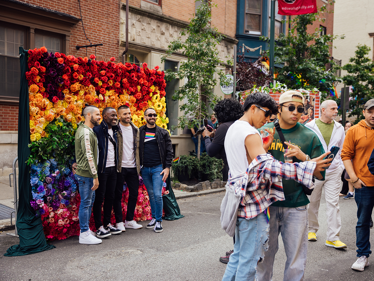 Les participants au festival posent devant un mur fleuri aux couleurs vives de l'arc-en-ciel tandis que d'autres prennent des selfies pendant le OURfest.