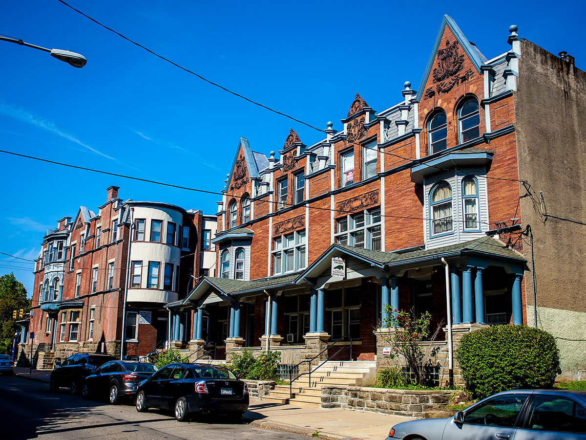 Victorian-style red-brick row homes in the Powelton Village neighborhood in Philadelphia, with blue-trimmed bay windows, pointed gables and decorative stonework.