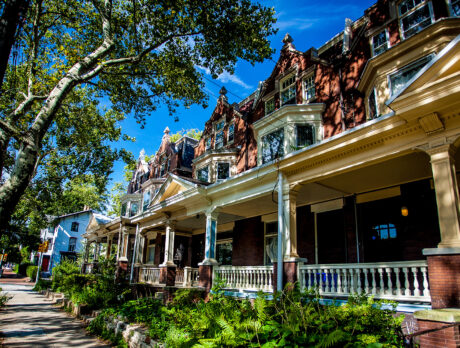 A tree-lined street in Powelton Village with historic brick row homes featuring porches, columns and ornate rooflines.