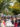 Crowds gather at long picnic tables and vendor tents during an outdoor street festival, with people eating, shopping and enjoying the lively atmosphere.