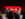 Audience members face a stage where a bright red TED sign glows against a dark red curtain backdrop.