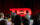 Audience members face a stage where a bright red TED sign glows against a dark red curtain backdrop.