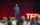 A man in a blue suit speaks in front of a seated audience during a TED Democracy Fireside Chat event, standing near a red TED sign against a dark red curtain backdrop.