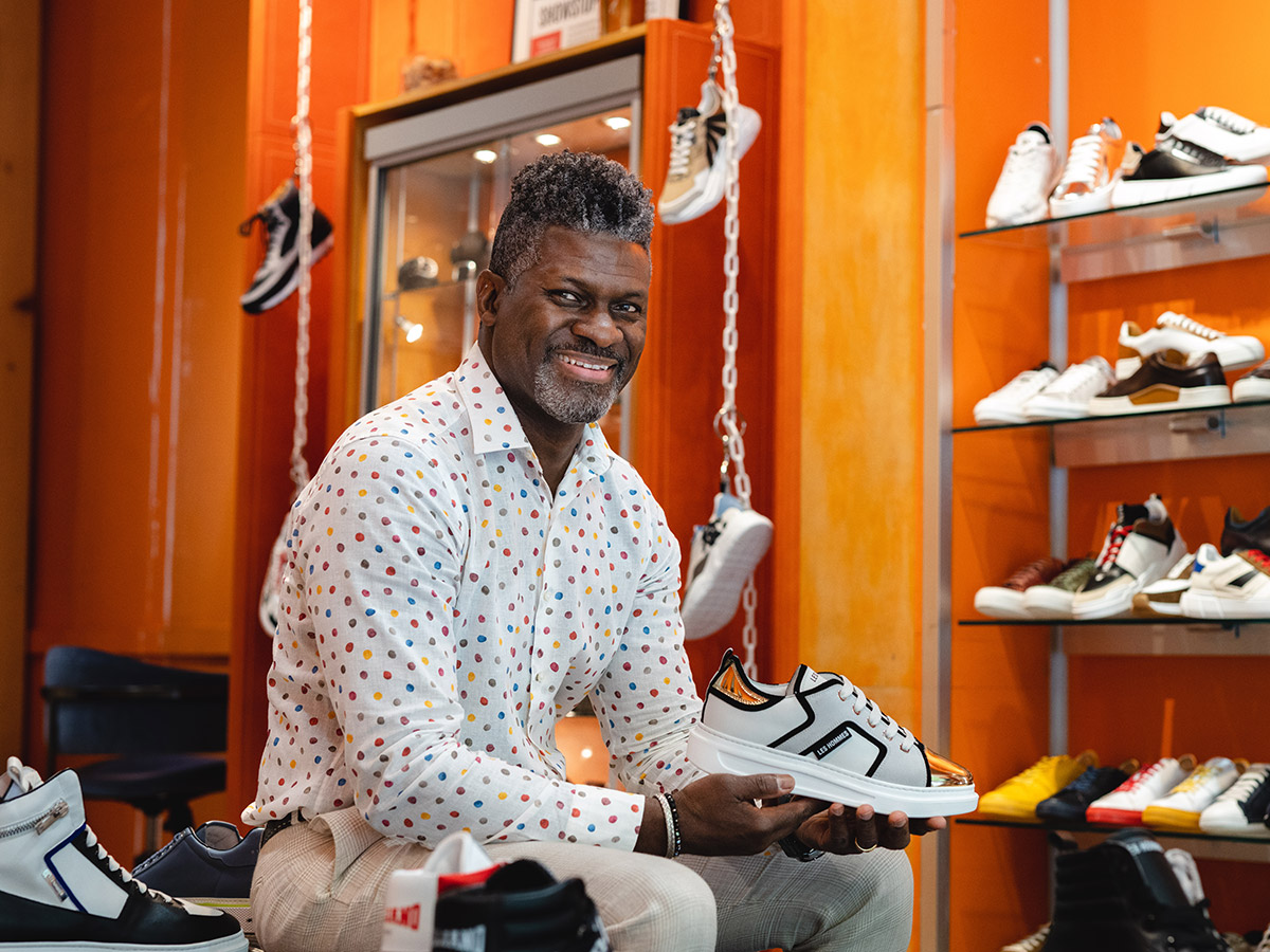 Dressed in a polka dot shirt and surrounded by sneakers, the owner of Blue Sole Shoes smiles at camera