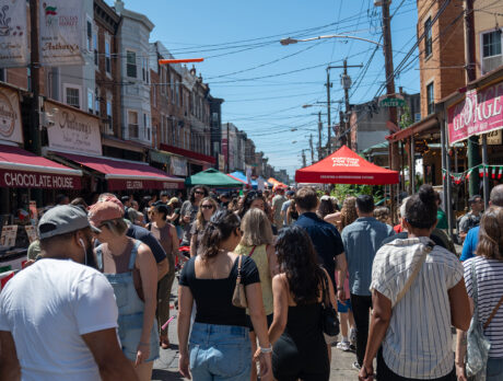 A crowd of people pack the South 9th Street Italian Market, browsing vendor stalls under colorful tents and signs during the Italian Market Festival.