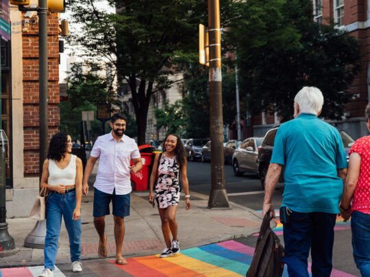People cross a street in Philadelphia that has a rainbow crosswalk.