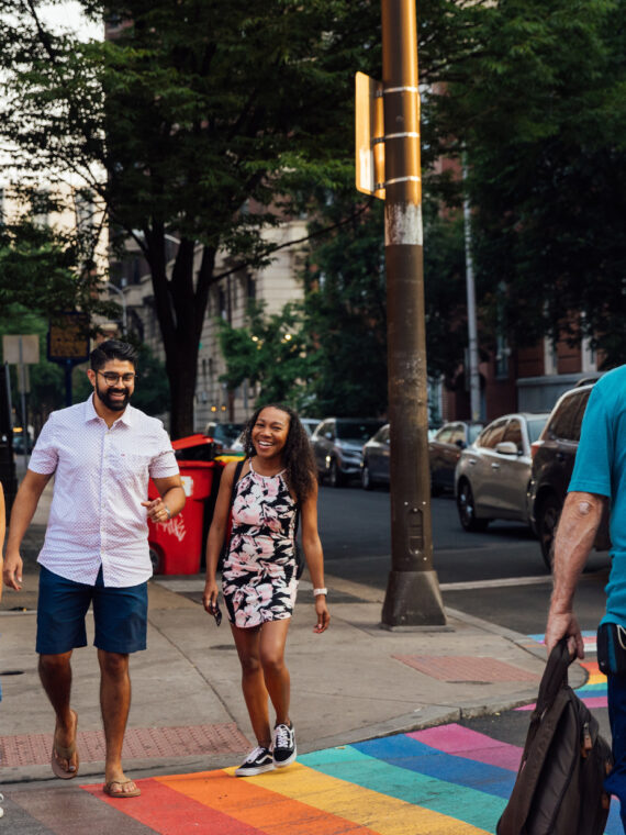 People cross a street in Philadelphia that has a rainbow crosswalk.