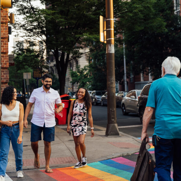People cross a street in Philadelphia that has a rainbow crosswalk.