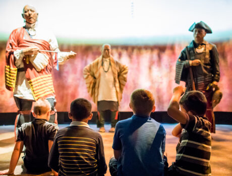 A group of children sit on the floor watching live-history figures in the Oneida Nation Theater at the Museum of the American Revolution.
