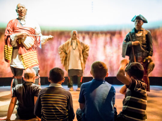 A group of children sit on the floor watching live-history figures in the Oneida Nation Theater at the Museum of the American Revolution.
