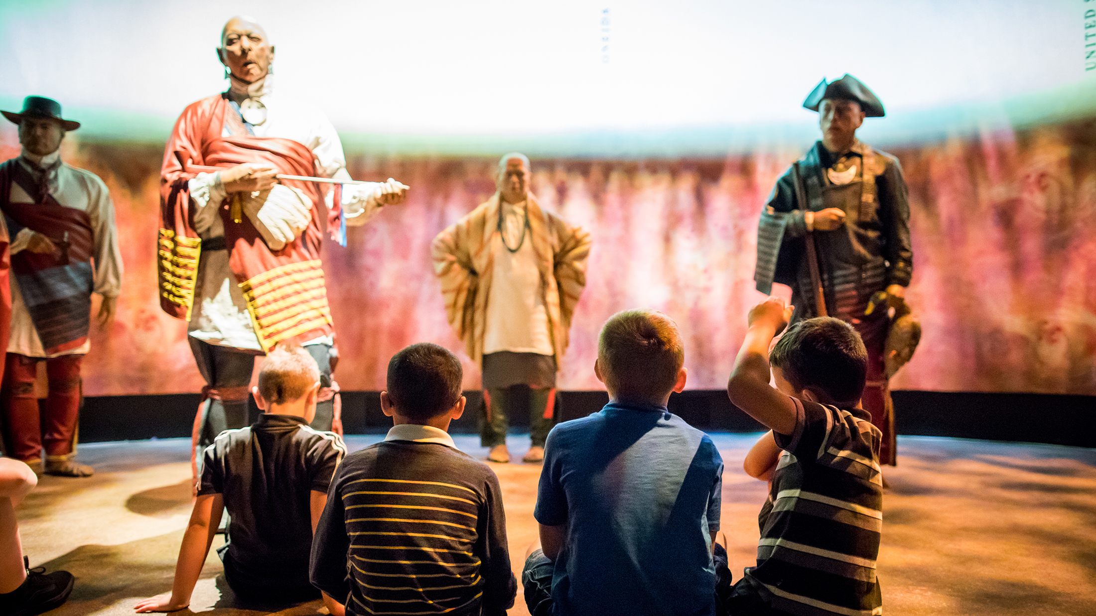 A group of children sit on the floor watching live-history figures in the Oneida Nation Theater at the Museum of the American Revolution.