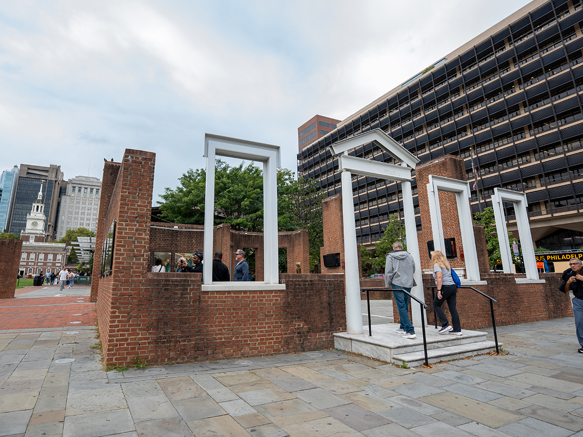 Visitors explore the open-air President's House Site featuring partial brick walls and white architectural frames marking the home's historic footprint.