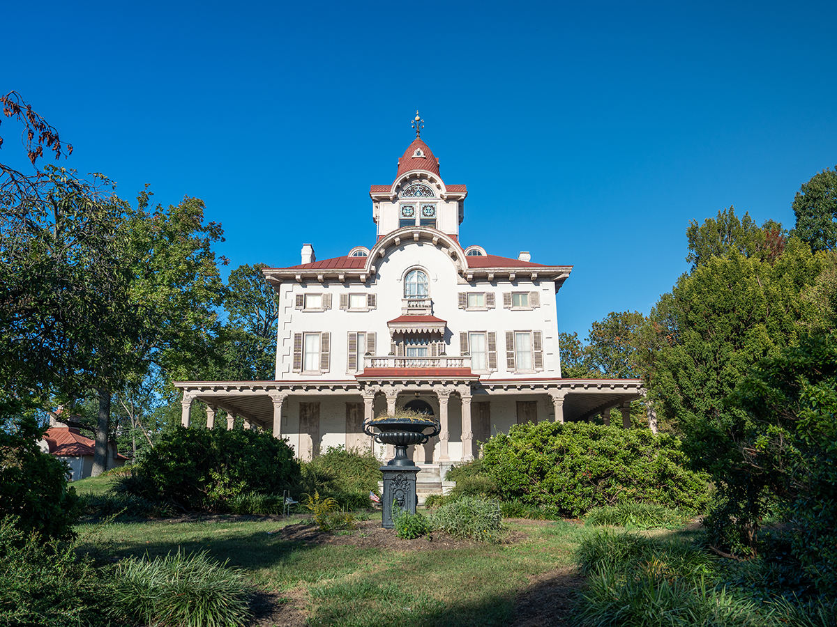 The exterior of Ryerss Museum and Liberty. A grand 19th-century mansion with a red roof and clock tour surrounded by lush greenery under a blue sky.